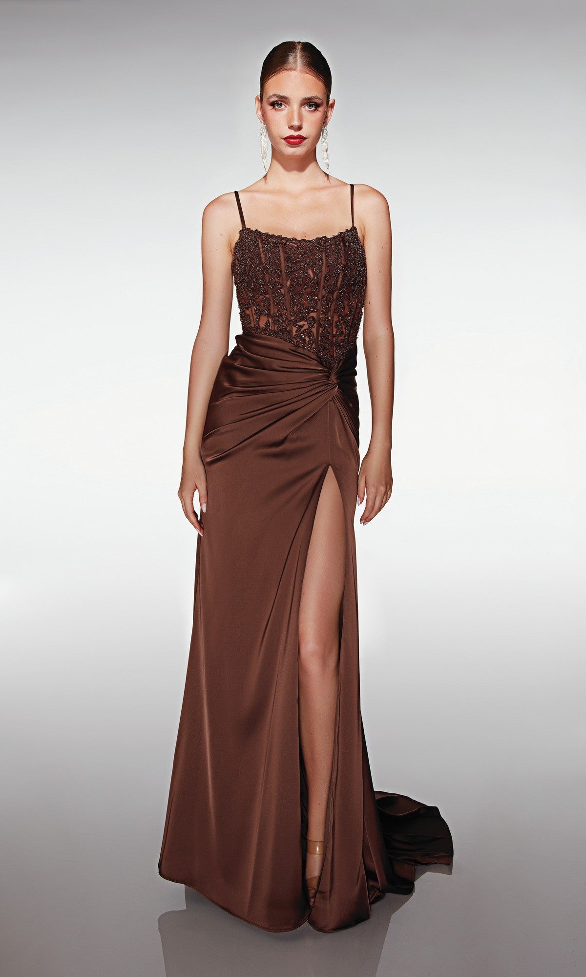 A woman wearing the Aerie Couture 376 long prom dress in chocolate, featuring an embroidered corset bodice, thin straps, ruched waist, and a high leg slit, stands against a plain light background.